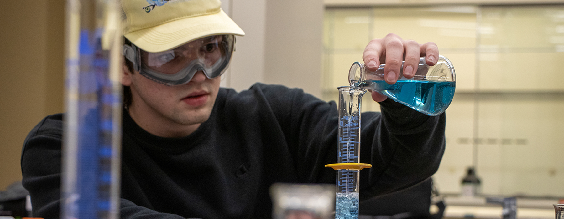 student pouring a blue liquid into a glass test tube