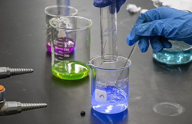 lab student with several beakers full of bright colorful liquids